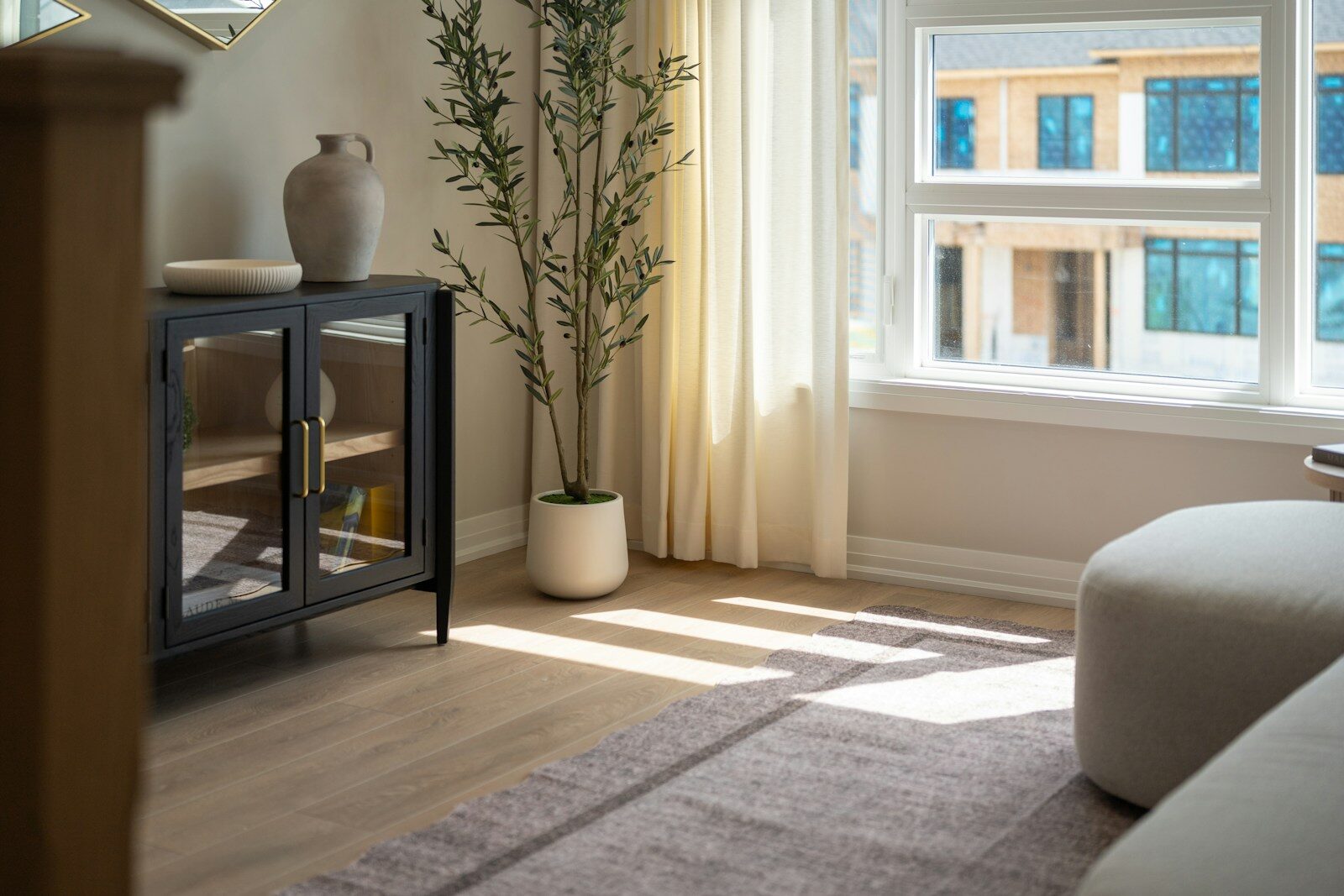 Photo by Franco Debartolo A black cabinet with glass doors beside a potted olive tree in a living room